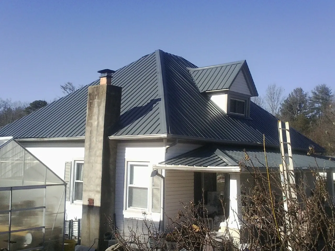 Dark blue standing seam metal roof on a white farmhouse with dormer — Slate & Tile Roof Repair by Roofing Brothers in Black River Falls