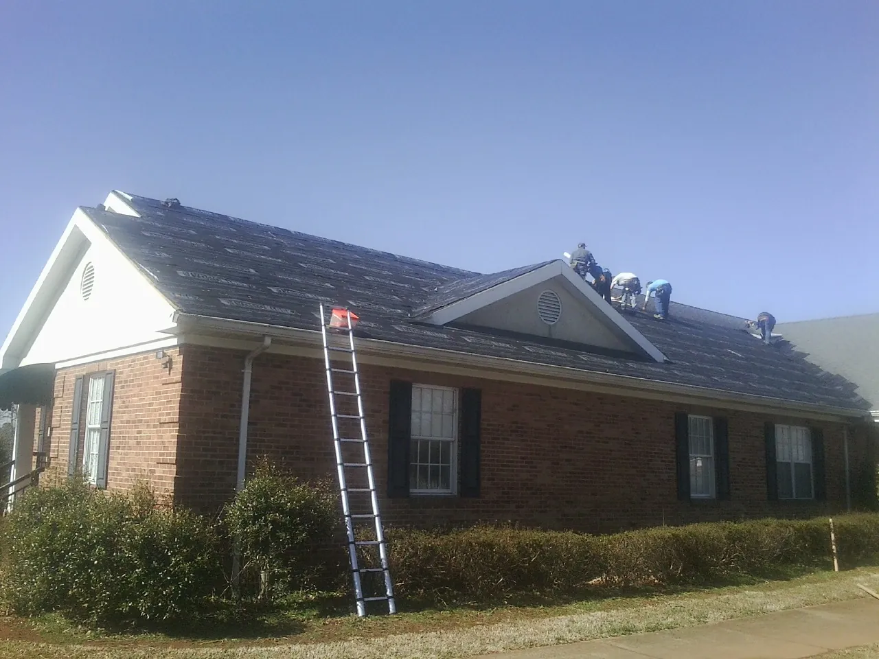 Crew tearing shingles off a brick ranch roof with a ladder set — Emergency Roof Repair work by our crew in Black River Falls
