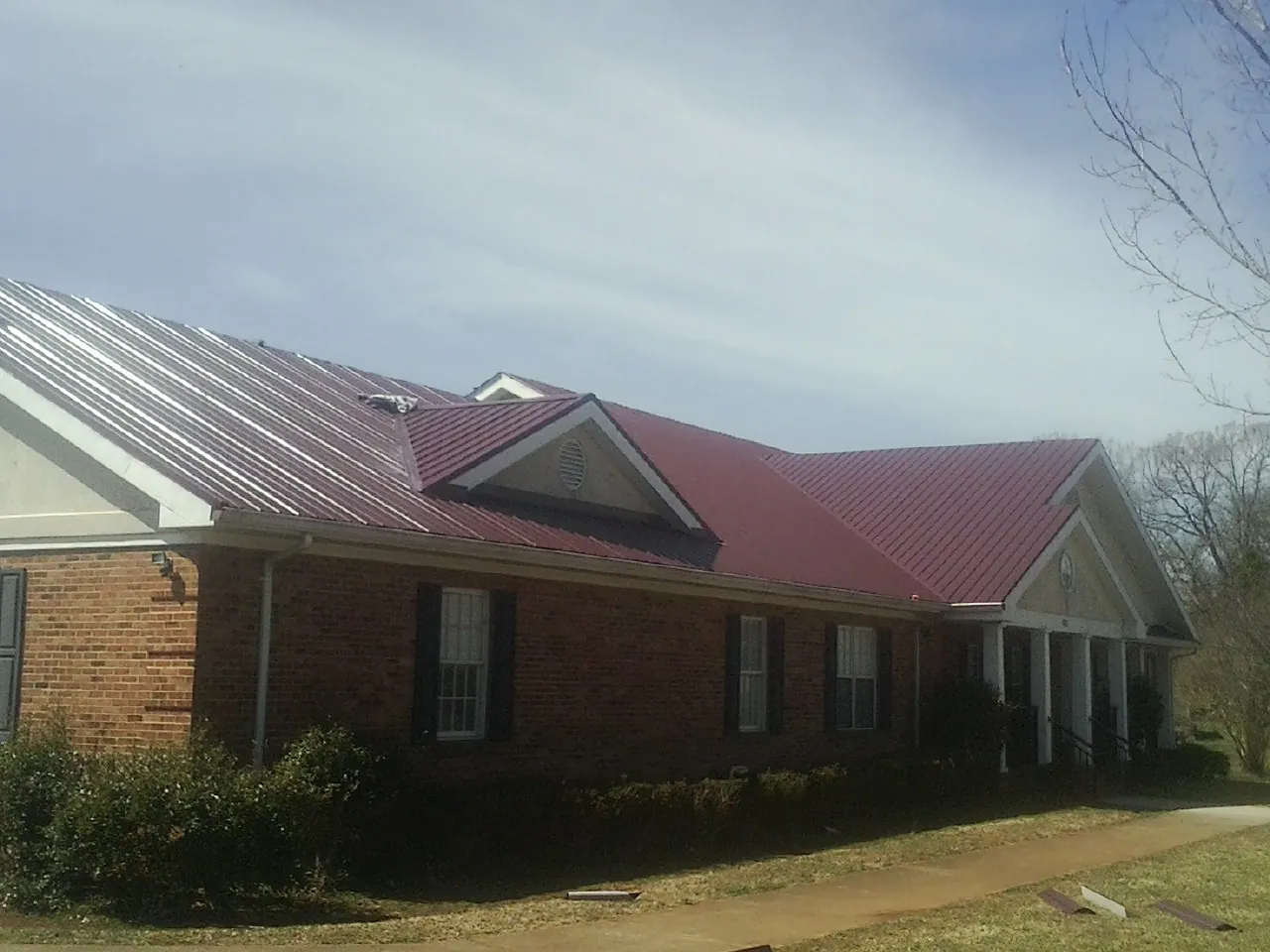 Red metal roof with gabled entries on a long brick building, from a Hail Damage Roof Repair job in Black River Falls