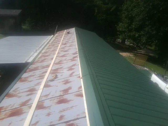 Old rusted panels beside newly installed green metal roofing — Wind Damage Roof Repair by Roofing Brothers in Black River Falls