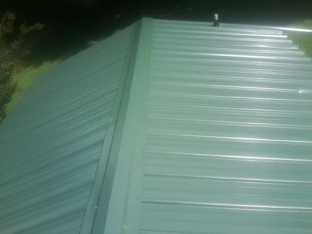 New green metal panels meeting at the ridge of a roof — Flat Roof Repair work by our crew in Black River Falls