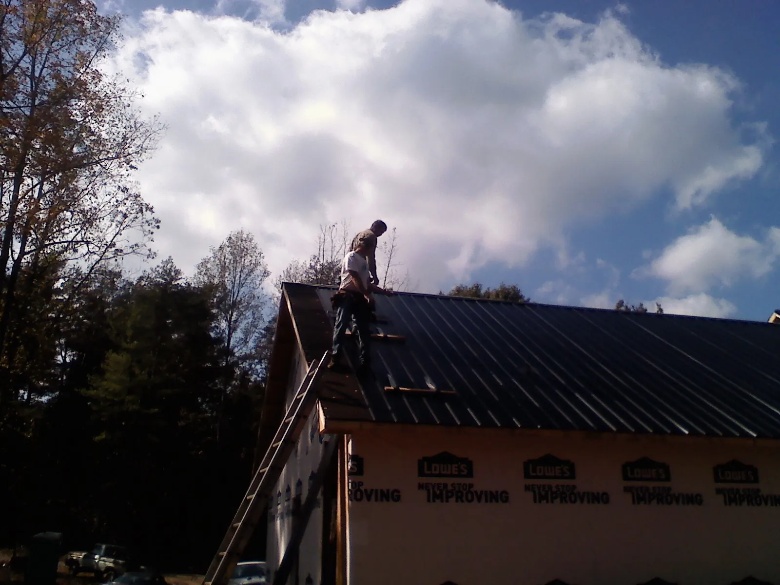 Roofer fastening dark metal panels high against a cloudy sky, from a Roof Inspection job in Black River Falls