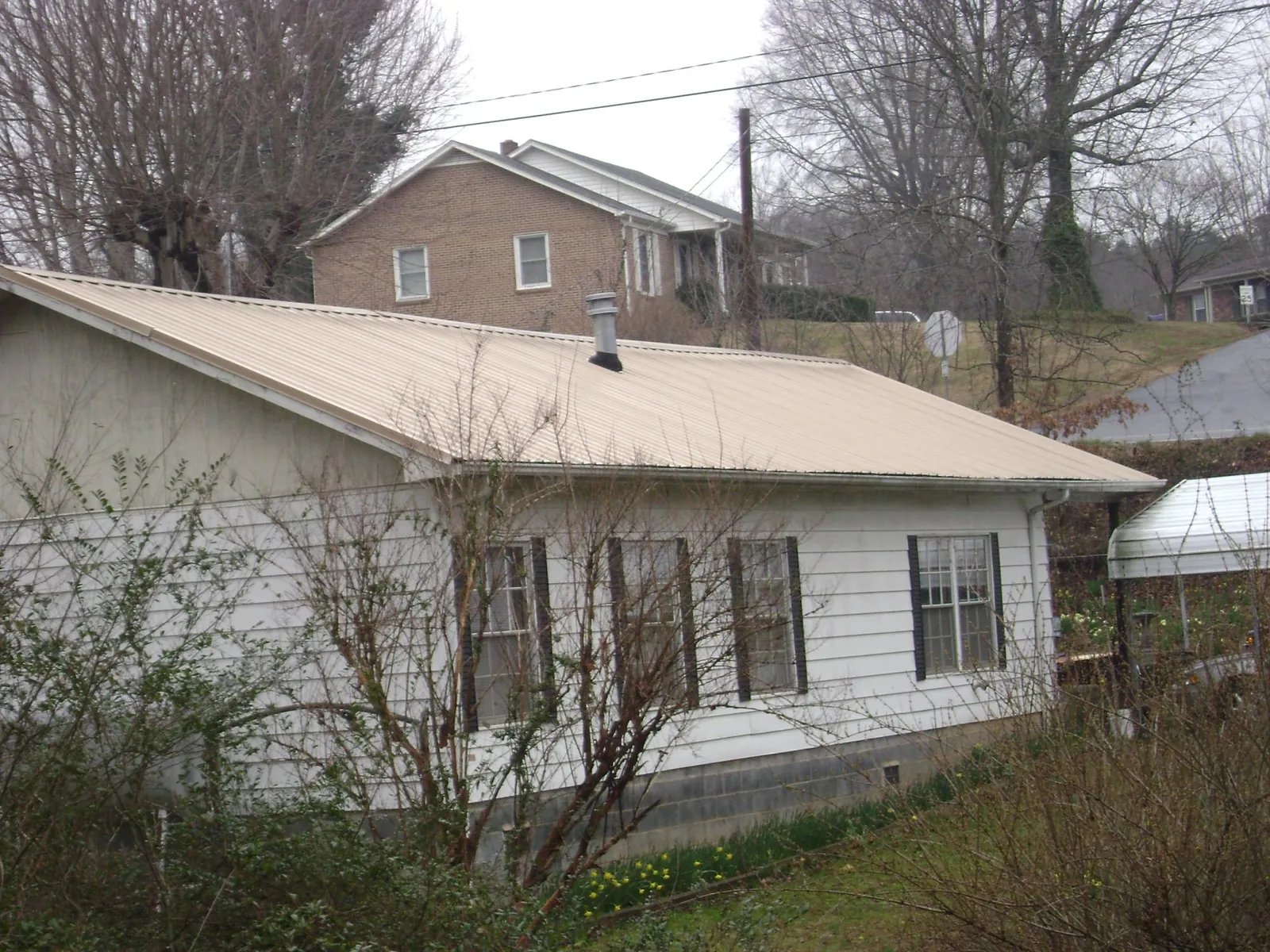 Tan metal roof on a white sided house set into a hillside — Commercial Roofing by Roofing Brothers in Black River Falls