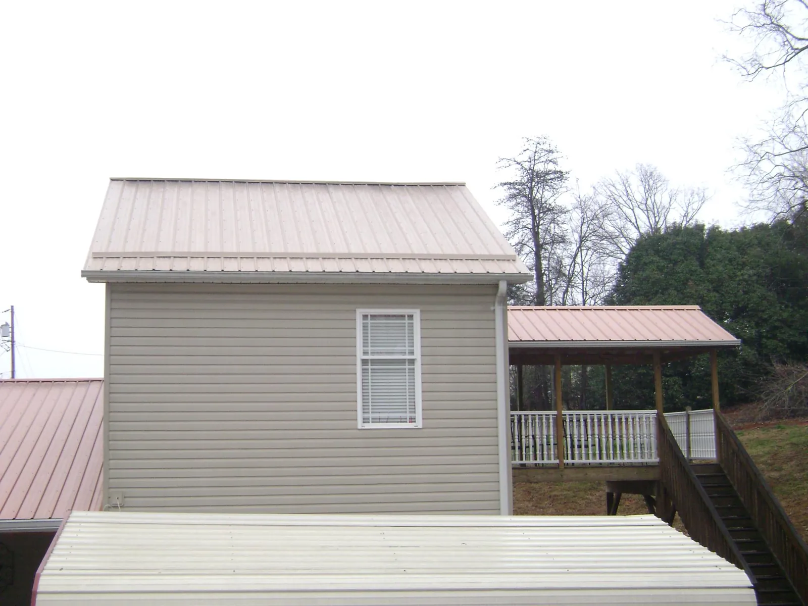 Tan metal roofs on a two story addition and attached porch, from a Roof Replacement job in Black River Falls