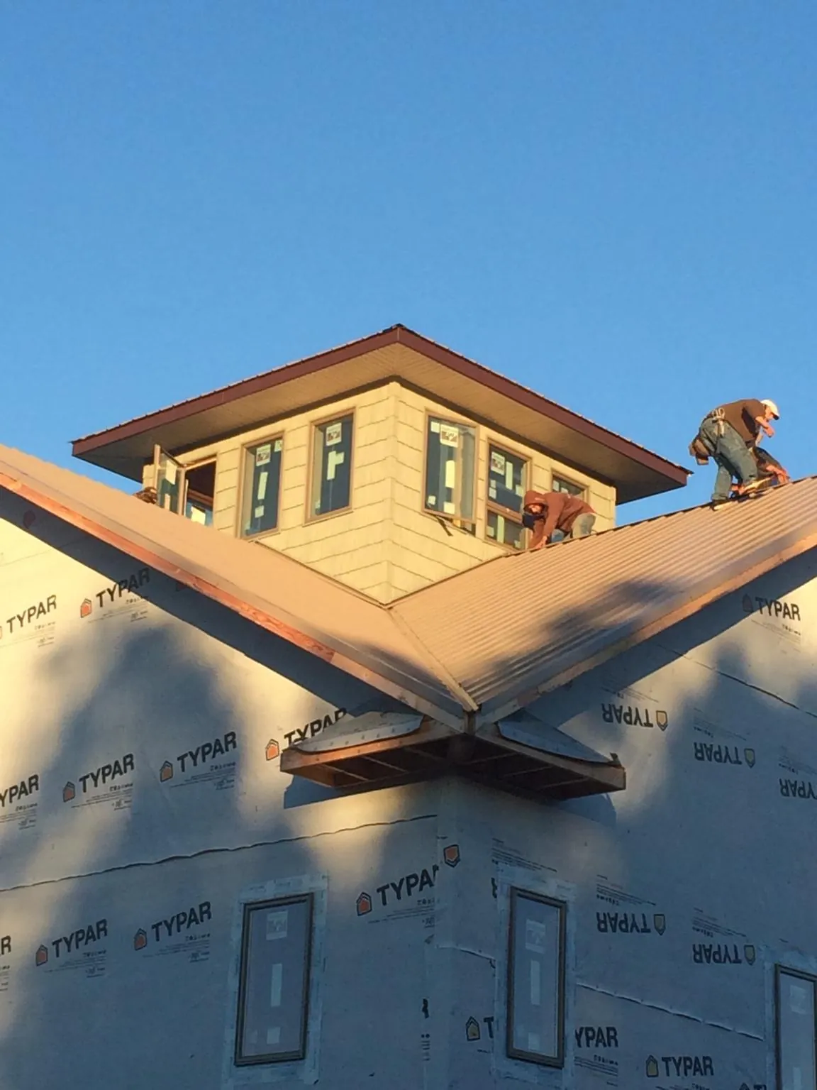 Roofers working around a rooftop cupola on a new metal roof at sunset — Roof Waterproofing in Black River Falls by Roofing Brothers